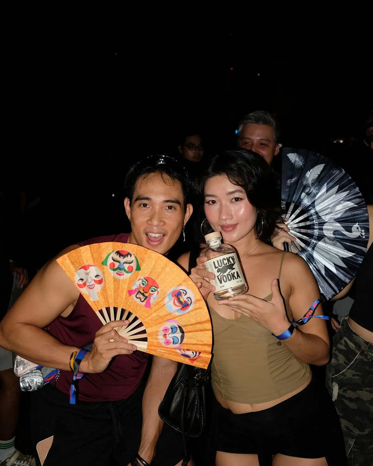 Two friends with hand fans holding a bottle of Lucky Vodka