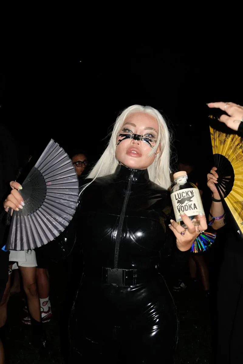 A girl in black latex holding a bottle of Lucky Vodka