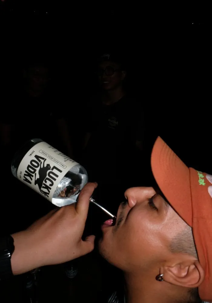 A guy drinking straight from a bottle of Lucky Vodka