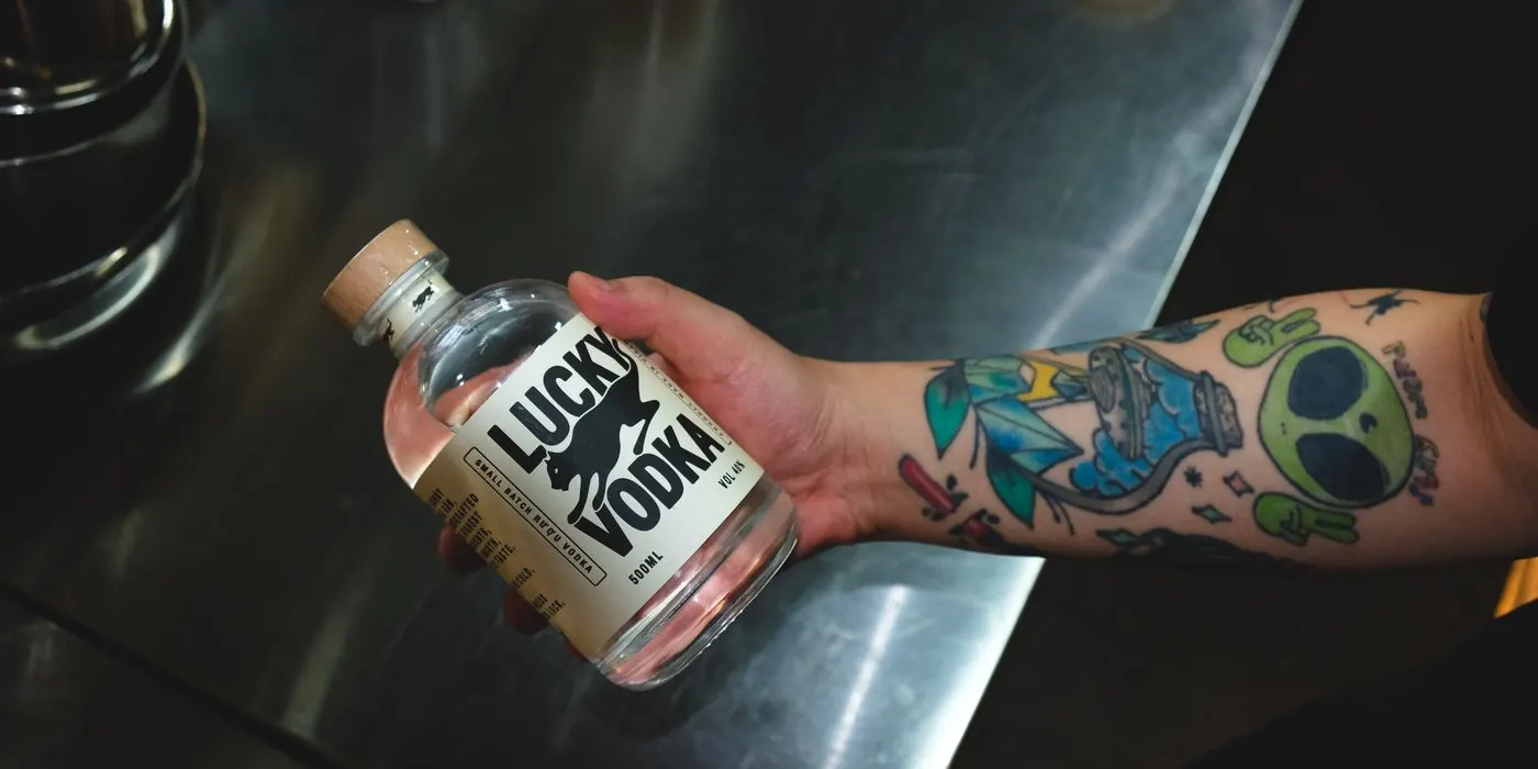 A tattooed hand holding a bottle of Lucky Vodka