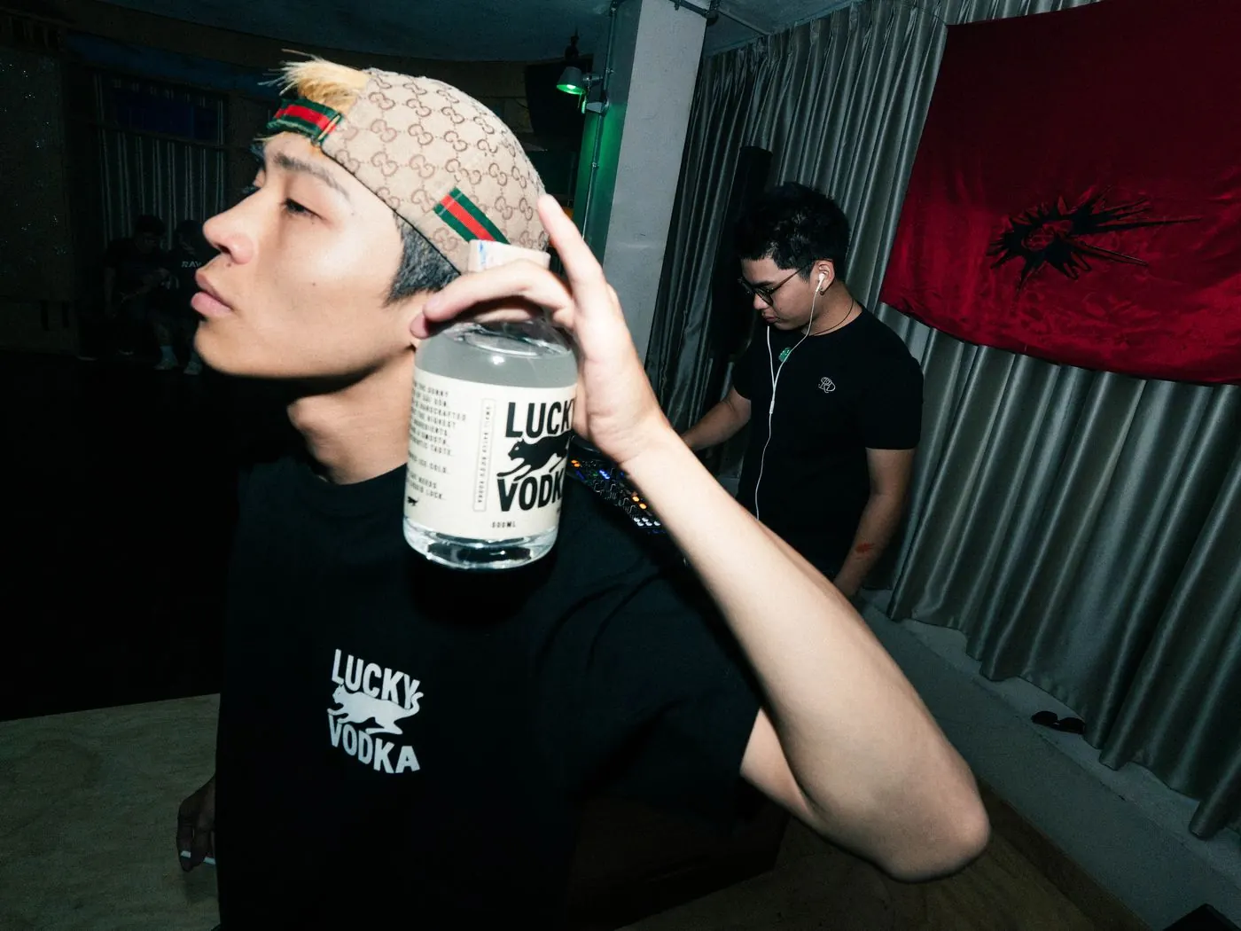A guy holding up a bottle of Lucky Vodka at a venue
